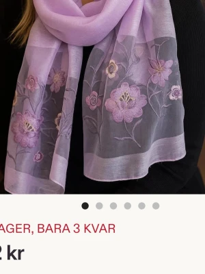 Ljuslila sjal med broderade blommor - Söt ljuslila sjal i tunt, transparent tyg med broderade blommor i olika lila nyanser. Sjalen har en rektangulär form och blommönstret ger en romantisk och trendig känsla. Perfekt att slänga över axlarna för en extra touch till din outfit.