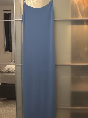 Ljusblå långklänning med tunna band - Säljer en elegant ljusblå långklänning med tunna axelband och rak siluett. Klänningen har en minimalistisk design och är perfekt för sommarens alla tillfällen. Materialet känns mjukt och svalt mot huden.