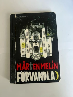 Förvandlad av Mårten Melin - Ene spännande skönlitterär bok med svart hård pärm och ett mystiskt slott på framsidan. Titeln 'Förvandlad' och författaren Mårten Melin står i stora bokstäver. Perfekt för dig som gillar mysterier och internatskolemiljöer.