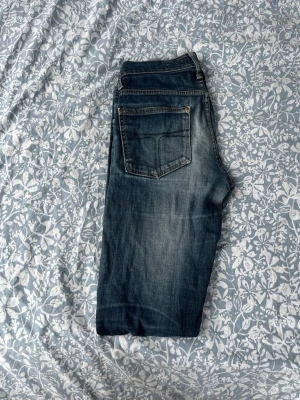 Mörkblå raka jeans med slitningar - Säljer ett par mörkblå jeans med raka ben och snygga slitningar på framsidan. Jeansen har klassisk femficksdesign och kontrastsömmar. Perfekta för en avslappnad och trendig look. Materialet är denim i bomull.