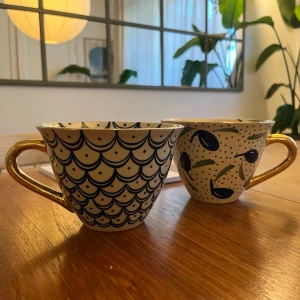 Temugg, Kerstin Tillberg  - Två stycken stora temuggar av keramikern Kerstin Tillberg. Muggarna är i gott skick och har fina detaljer i guld på örat. Muggarna är otroligt härliga att dricka ur och är perfekt för den som gillar att dricka den stora koppen med te. 