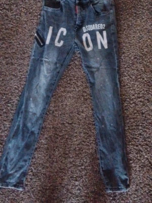 Dsquared2 ICON jeans i blå denim - Snygga blå jeans från Dsquared2 med vit 'ICON'-text framtill. Jeansen har en smal passform och klassisk femficksdesign. Tuffa detaljer och slitningar ger en trendig look. Perfekta för dig som vill sticka ut med din stil.