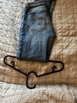 Blå slim fit jeans från Nudie - Säljer ett par klassiska blå slim fit jeans från Nudie Jeans med snygga kontrastsömmar och femficksmodell. Jeansen har en normalhög midja och är tillverkade i mjuk denim med lätt tvättad look. Perfekta till vardagsstilen! Det står i strl w30 l32 men dem har krymt så passar även w27 och uppåt. Väldigt bra skick, skriv vid frågor.