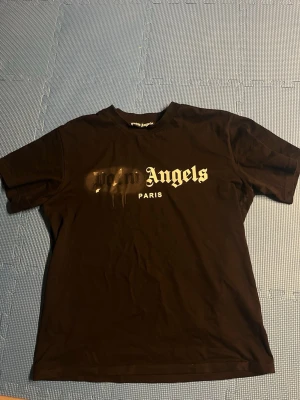  Palm Angels - Säljer en svart t-shirt från Palm Angels med trycket 'Palm Angels Paris' i vitt framtill. T-shirten har korta ärmar och klassisk passform. Materialet är mjuk bomull och trycket har en cool drip-effekt över loggan.