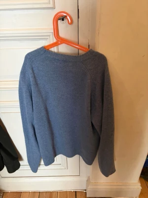 Blå stickad tröja från Uniqlo - Mysig blå stickad tröja från Uniqlo med rund halsringning och långa ärmar. Tröjan har en enkel och stilren design, perfekt för lager på lager. Materialet ser ut att vara mjukt och bekvämt, och modellen är något lösare för en avslappnad look.
