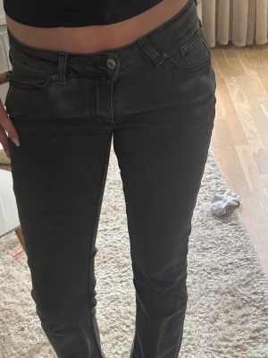 Mörkgråa bootcut jeans med låg midja - Säljer ett par gråa bootcut jeans med låg midja och klassisk femficksdesign. En extraknapp är ditsatt för dom var lite stora i midjan