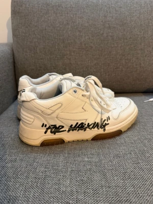 Off-White vita sneakers med text - Säljer ett par vita Off-White sneakers med svart texten 'For Walking' på sidan. Skorna har klassisk låg siluett, vita snören och detaljer i läder. Snygg Off-White-logga på plösen och insidan. Perfekta för dig som gillar streetwear och unika detaljer.