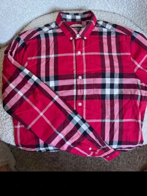 Burberry Brit rutig skjorta – Strl S – Mycket fint skick - Säljer en jättefin, klassiskt rutig herrsskjorta från lyxmärket Burberry (Burberry Brit). Storlek: S (Slim fit)  Material: 100% bomull  Skick: Mycket gott skick, välvårdad och utan fläckar eller defekter.  Klassiskt Burberry-mönster i rött, rosa, svart och vitt. Perfekt till både vardag och finare tillfällen.  Kommer från ett djur- och rökfritt hem. Kan skickas spårbart!