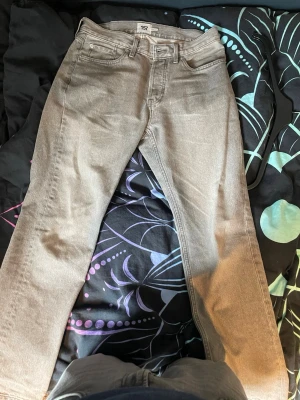 Grå raka jeans från lager 157 - Säljer ett par grå jeans från 157 med rak passform och klassisk femficksdesign. Jeansen har bälteshällor, knappgylf och är tillverkade i ett slitstarkt denimtyg. Perfekta för en avslappnad och stilren look.