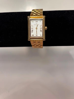Mockberg klocka - Elegant guldfärgad klocka från Mockberg. Klockan har en stilren rektangulär urtavla med romerska siffror och ett klassiskt guldfärgat armband som passar både till vardag och fest.    Den är i fint skick och ger en väldigt lyxig och tidlös känsla. Perfekt accessoar om du vill ha en minimalistisk men elegant look.    Batteriet behöver bytas. Missfärgningar på lister, men syns knappt (kan skickar bilder)!  ✨ Märke: Mockberg   ✨ Färg: Guld   ✨ Modell: Rektangulär urtavla med romerska siffror  