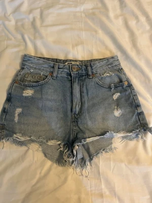 Högmidjade ljusblå jeansshorts - Säljer ett par högmidjade ljusblå jeansshorts från FIVE UNITS med slitna detaljer och fransig kant. Klassisk femficksmodell med knapp och dragkedja framtill. Perfekta för sommaren och ger en avslappnad vibe.💗