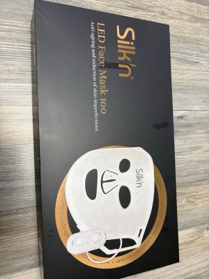 Silk'n LED Face Mask 100 - LED Face Mask 100 från Silk'n, en vit ansiktsmask i plast med inbyggda LED-lampor för hudvård. Masken har utskärningar för ögon och näsa samt justerbart band och fjärrkontroll. Perfekt för behandling av hudproblem och anti-aging. Kostar 1 700kr ny. Nästan aldrig använt 