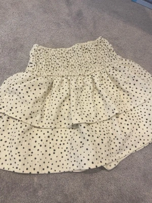 Prickiga skorts med volanger - Supersöta skorts i beige färg med svarta prickar och volangdetaljer. Har bred resår i midjan för skön passform och shorts under kjoldelen. Perfekt för dig som vill ha både stil och bekvämlighet. Materialet känns lätt och luftigt.