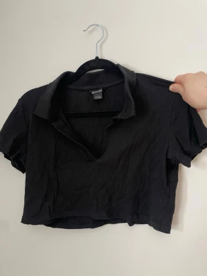 Svart croppad ribbad topp Monki - Snygg men kort festtopp! Skulle säga att den mer är en M än en L. Dessvärre har sömmen längst ner gått sönder på en del av tröjan, men det är enkelt att åtgärda.