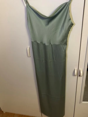 Balklänning från Vila - Säljer en elegant ljusgrön balklänning från Vila med tunna axelband och mjukt, glansigt material. Klänningen har en vacker draperad urringning och en smickrande, rak passform. Justerbara band.