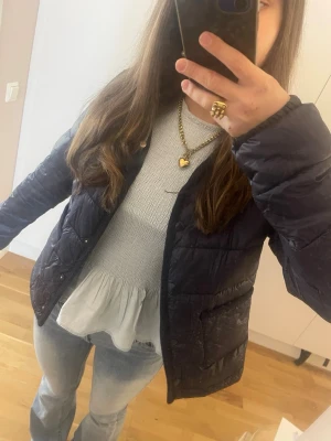 Mörkblå pufferjacka  - Säljer en svart pufferjacka med lätt glansigt material och tryckknappar framtill. Jackan har två stora fickor och en enkel, rak passform som ger en clean look. Perfekt till våren  och enkel att matcha med olika outfits. Storlek 170 men passar som XS 