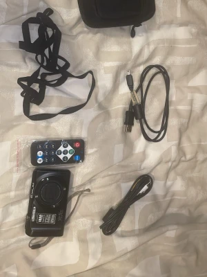 Casio Exilim svart digitalkamera - Säljer en svart Casio Exilim digitalkamera med 12,5x optisk zoom, 16,1 MP och HD Movie-funktion. Kameran är kompakt och har en stilren design i plast och metall. Medföljer fjärrkontroll, rem, kablar och väska. Perfekt för dig som vill ta snygga bilder och filmer.