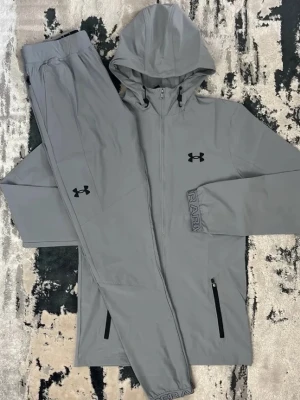 Gråa mjukisbyxor från Under Armour - Säljer ett par gråa mjukisbyxor från Under Armour med resår i midjan och diskret logga på benet. Byxorna har en avslappnad passform och är tillverkade i ett mjukt, stretchigt material som känns skönt mot huden. Perfekta för chill eller träning.