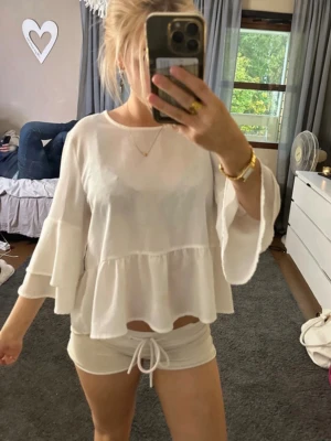 Vit volangblus med vida ärmar - Säljer en luftig vit blus med volangdetaljer och vida, långa ärmar. Blusen har en lös passform.