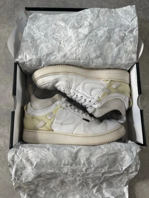 Nike Air Force 1 x Undercover vita - Nike Air Force 1 x Undercover sneakers i vitt läder med Undercover detaljer i beige och genomskinlig plast. Klassisk swoosh på sidan, Undercover textdetaljer och robust sula. 