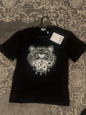 Svart Kenzo t-shirt med tigertryck - Svart t-shirt från Kenzo med ikoniskt tigertryck och texten 'KENZO PARIS' på bröstet. Storlek S men passar också med M