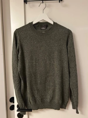 Grön stickad tröja Oscar Jacobson - Snygg grönmelerad stickad tröja från Oscar Jacobson. Klassisk rund halsringning och långa ärmar. Perfekt för en stilren och enkel look.