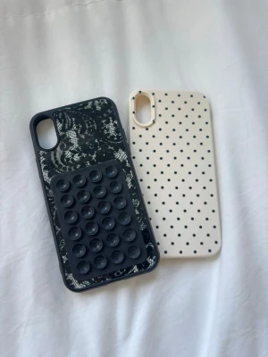 Två mobilskal med mönster💗 - Säljer två snygga mobilskal till iPhone. Ett svart skal med spetsmönster och som har sugproppar på, och ett vitt skal med små svarta prickar. Båda är tunna och flexibla, perfekta för dig som vill ha ett personligt skydd till mobilen. Passar iPhone X, XS, XR💗 har inga defekter och är som helt nya! Går att köpa tillsammans för 99 kr eller för 75 kr separat!