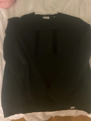 Svart sweatshirt från Les Deux - Snygg svart sweatshirt från Les Deux med diskret ton-i-ton tryck på bröstet. Klassisk rund halsringning och ribbade muddar vid ärmslut och nederkant. Perfekt till jeans eller chinos för en clean look.