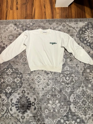 Vit sweatshirt med tryck från Valient - Vit sweatshirt med rund halsringning och tryckt logga i grönt på bröstet från  Valient. Perfekt för en avslappnad och stilren look. Tröjan är använd ett fåtal gånger och är i gott skick. 