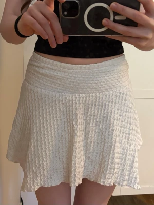 Vit våfflad minikjol med struktur - Säljer en vit minikjol med våfflad struktur och elastisk midja. Kjolen har en lätt utsvängd passform och vågig textur i tyget. 