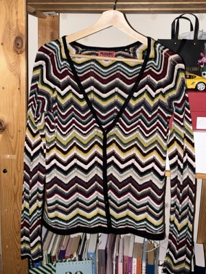 Missoni Lindex zigzag kofta S - Snygg långärmad kofta från Missoni Lindex i storlek S. Koftan har ett ikoniskt zigzag-mönster i vinrött, gult, svart, vitt och blått. Tunn stickning med glittriga inslag och svarta kanter. Perfekt för att lyfta vilken outfit som helst.