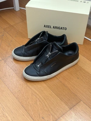 Svarta sneakers Axel Arigato zip - Arigato Clean 90’s med zip, använda ett fåtal gånger och är i fantastiskt skick, storlek 42. Box ingår. Hör gärna av vid frågor!