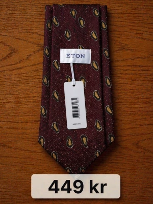 Brun paisleymönstrad slips från Eton - Snygg brun slips från Eton med paisleymönster i gult och svart. Slipsen har en klassisk form och är tillverkad i ett elegant tyg som ger en exklusiv känsla. Perfekt för dig som vill addera lite extra stil till outfiten. Nypris ca 1000–1500 kr/st – säljes till riktigt bra pris. 