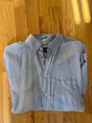 Ljusblå skjorta från Eton - Klassisk ljusblå skjorta från Eton med button down-krage och bröstficka. Skjortan har långa ärmar och vita knappar framtill. Perfekt nu mot sommaren då den är väldigt sval och stilren. Ordniarie pris runt 1200kr. Priset kan diskuteras. Storleken passar L bra också