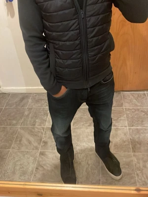 Svart cardigan  med dragkedja från dressman - Säljer en svart cardigan med quiltat mönster och dragkedja framtill. Jackan har två fickor med lock och släta ärmar i sweatshirtmaterial. Perfekt för våren/ hösten och sommaren och ger en clean, modern look.