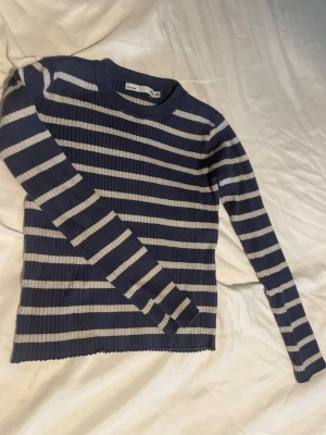 Blårandig stickad tröja från lager 157 barn st 140 - Randig stickad tröja från lager 157 i blått och vitt. Tröjan har ribbstickad struktur, rund halsringning och långa ärmar. Perfekt för dig som gillar klassiska ränder och enkel stil. Barn storlek 140