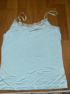 Ljusblå linnetopp med spetskant - Söt ljusblå linnetopp med tunna axelband och dekorativ spetskant upptill. Perfekt för varma dagar eller som lager under en tröja. Enkel och stilren design som passar till det mesta.
