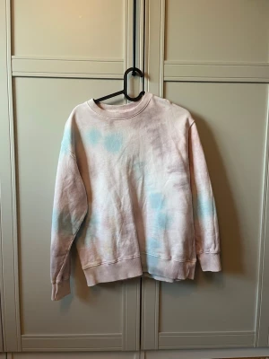 Pastellfärgad sweatshirt från Zara - Säljer en oversized sweatshirt från Zara i pastellfärgad tie-dye med ljusrosa och blå toner. Tröjan har rund halsringning, ribbade muddar och är tillverkad i mjuk bomull. Perfekt för en chill och avslappnad stil.
