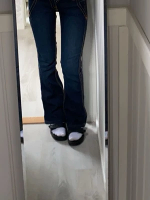 Mörkblå bootcut jeans med kontrastsömmar - Säljer ett par mörkblå bootcut jeans med tydliga kontrastsömmar och klassisk femficksmodell. Jeansen har låg midja och utsvängda ben, vilket ger en snygg retrovibe. Perfekta till sneakers eller boots för en avslappnad look. #nyskick #secondhand #marinblå #trendig #true religion 