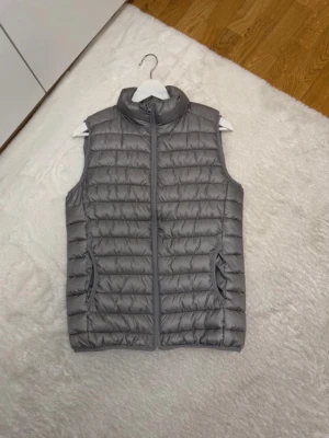 Primark väst - Snygg grå väst med quiltad design och hög krage. Perfekt att slänga över en hoodie eller tröja för extra värme. Enkel och stilren look som passar till det mesta.