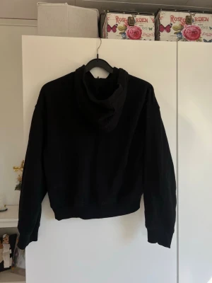 Svart hoodie med huva - En enkel och stilren svart hoodie med huva och långa ärmar. Hoodien har en klassisk passform och ribbade muddar vid ärmslut och nederkant. Perfekt för en avslappnad och bekväm look.