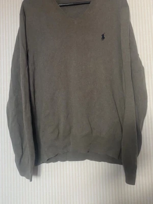 Olivgrön v-ringad tröja Polo Ralph Lauren - Olivgrön v-ringad tröja från Polo Ralph Lauren med diskret broderad logga på bröstet. Tröjan har långa ärmar och ribbade muddar vid ärmslut och nederkant. Perfekt för lager på lager och enkel att matcha med olika stilar.