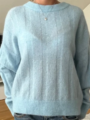 Ljusblå stickad mohairtröja - Mysig ljusblå stickad tröja i mohairblandning. Tröjan har en avslappnad passform, rund halsringning och diskreta lodräta ränder i stickningen. Perfekt för dig som gillar en soft och stilren look.