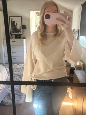 Beige stickad tröja med knytband - Säljer en beige stickad tröja med vida ärmar och snyggt knytband i midjan. Tröjan har rund halsringning och är gjord i ett mjukt, skönt material. Perfekt för dig som gillar en avslappnad men trendig stil.