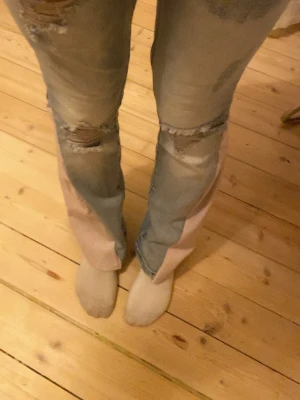 Ljusblå bootcut jeans med slitningar - Säljer ett par ljusblå och rosa bootcut jeans med slitna detaljer och hål på låren och knäna. Har då designat om dem till bootcut och sytt dem mer lågmidjade. 