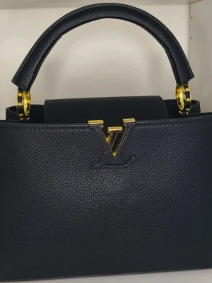 Capucines PM - Capucines PM i svart Taurillon-läder med guldfärgade detaljer. Storlek PM (31,5 × 20 × 11 cm). Strukturerad silhuett med handtag upptill och justerbar/avtagbar axelrem.  Skickbetyg: Utmärkt (10/10) – buren endast en gång. Äkta Taurillon-läder, perfekta detaljer.  Inkluderar dustbag och axelrem.