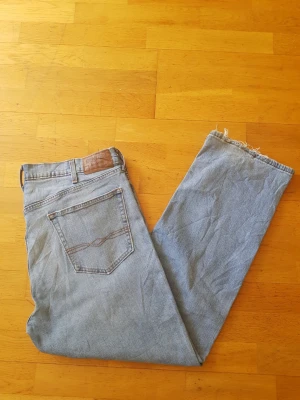 Ljusblå raka Levi's jeans - Säljer ett par klassiska ljusblå Levi's jeans med raka ben och råa, fransiga benslut. Jeansen har två bakfickor med den ikoniska sömmen och ett brunt läderpatch i midjan. Perfekta för en avslappnad och trendig look.