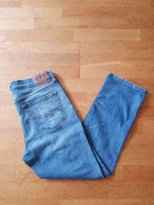 Levi's blå raka jeans Signature - Ett par klassiska blå jeans från Levi's Signature med raka ben och femficksmodell. Jeansen har en ljus tvätt och detaljerade sömmar på bakfickan samt en brun läderpatch i midjan. Perfekta för en avslappnad och tidlös stil.