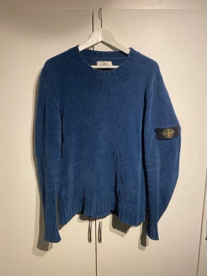 Stone Island Knitwear Blå - Säljer en blå stickad tröja från Stone Island med rund halsringning och ribbade muddar. Tröjan har den klassiska Stone Island-loggan på vänster ärm och är tillverkad i ett mjukt, grovt stickat material. Perfekt för dig som gillar streetwear och snygga detaljer. Storlek L och passar även M. fint skick, sparsamt använd. 