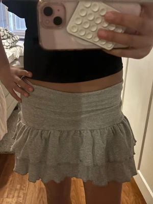 Grå volangkjol i bomull - Supersöt grå kortkjol med volangkant. Kjolen har en bred midjeresår och är gjord i mjukt bomullstyg som är bekvämt att bära. Perfekt till sommaren. Aldrig använt. Vet inte vart den är ifrån. Stork XS men passar typ alla storlekar för den är väldigt stretchig. Dock igen prislapp kvar.